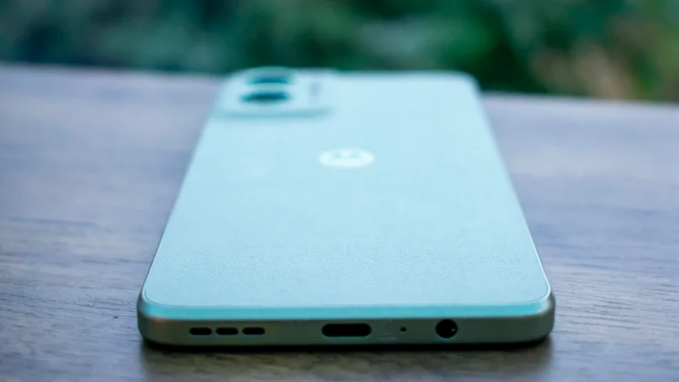 Motorola Moto G55 5G on a desk in front of a window, showing the bottom edge and charging port